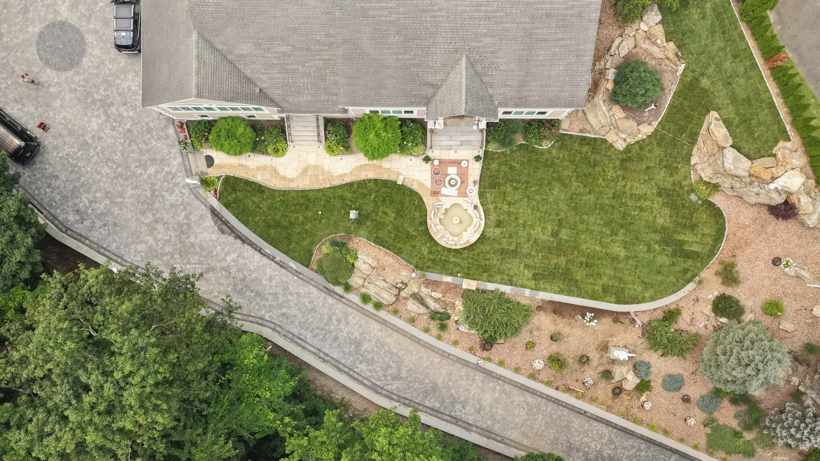 Straight-down drone view of the finished front yard in Shelton, CT — new sod cut cleanly around the fountain courtyard, walkway, and stone planting beds