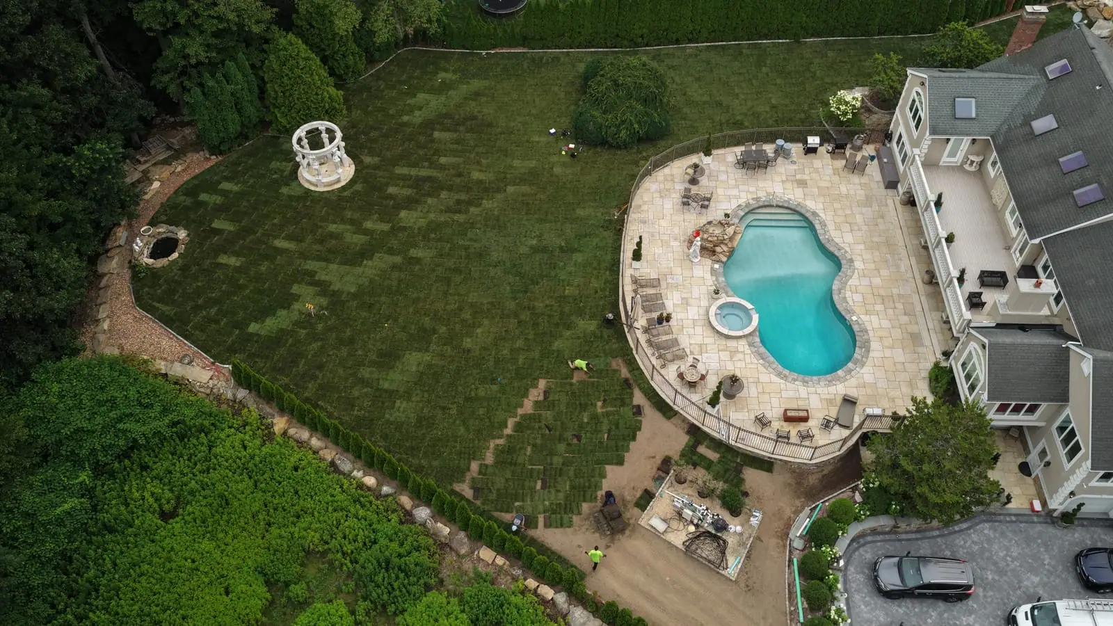 Aerial view midway through the Shelton, CT sod installation — laid sod advancing across the back yard while staged pieces fan down the slope toward the crew
