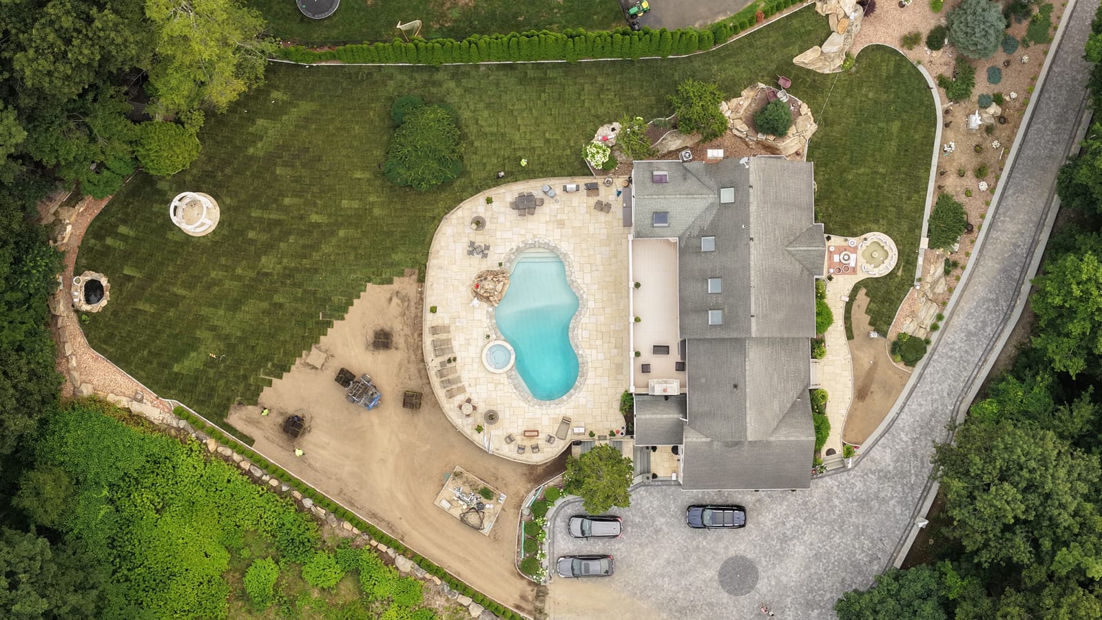 Straight-down drone view over the new pool and spa in Shelton, CT, with fresh sod installed across most of the yard and the final strip of graded soil beside the pool patio