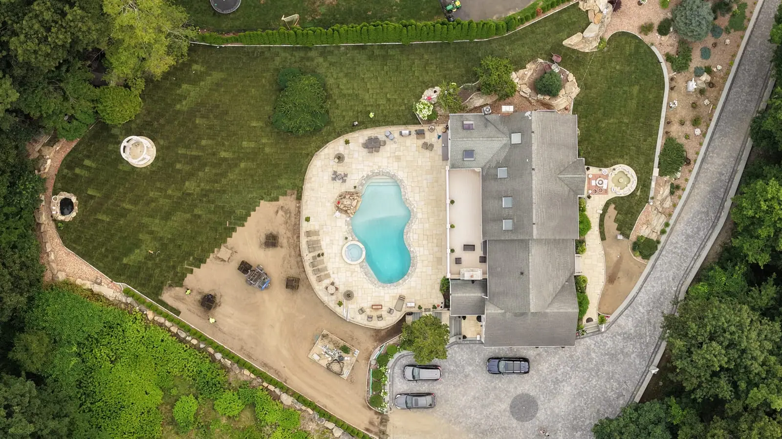 Straight-down drone view over the new pool and spa in Shelton, CT, fresh sod across most of the yard and the final strip of graded soil beside the patio