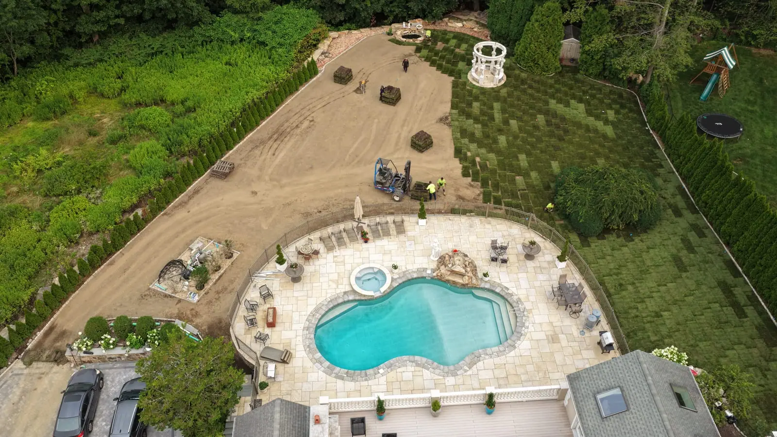 Aerial view over the new pool and spa in Shelton, CT as the crew and forklift work fresh sod across the yard toward the gazebo