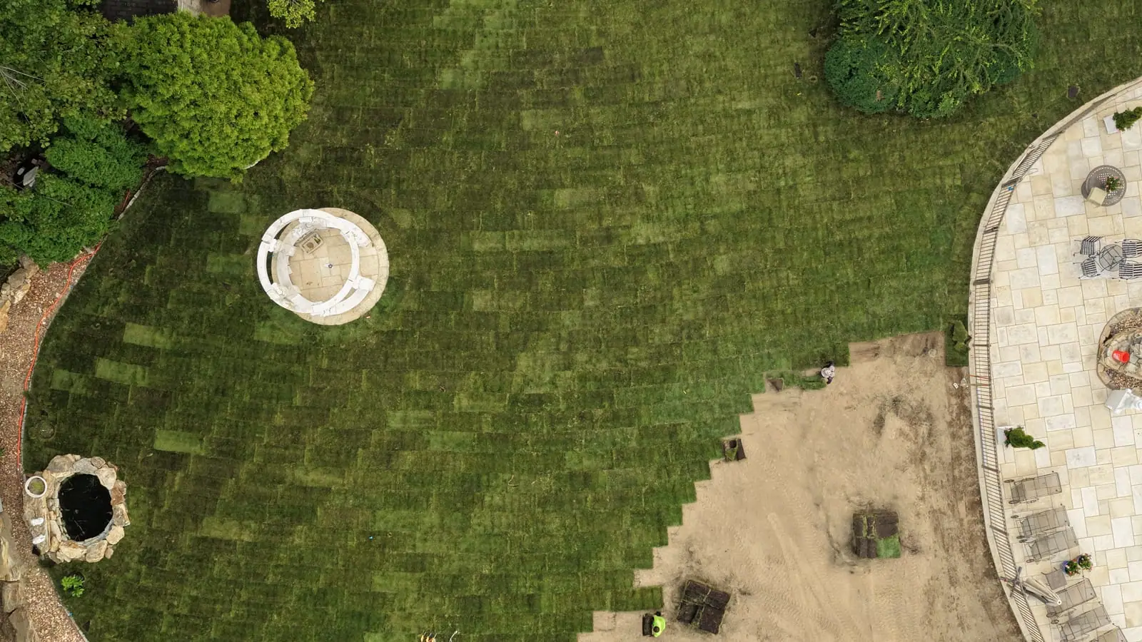 Overhead drone view of fresh sod rows laid around the white gazebo in Shelton, CT, the stair-stepped working edge meeting the remaining graded soil
