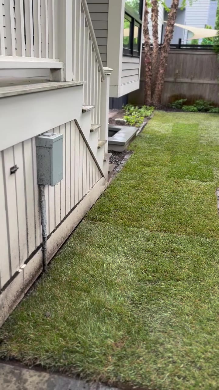 Finished walkthrough of the Cambridge backyard RTF sod install — clean seams along the foundation, tight cut against the river-rock drainage bed under the hot tub