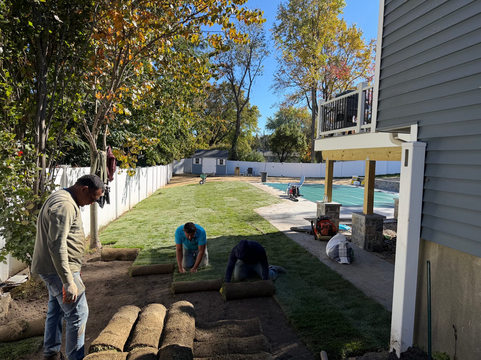 CT Sod crew laying sod in a Trumbull, CT backyard beside a covered pool, patio and raised deck