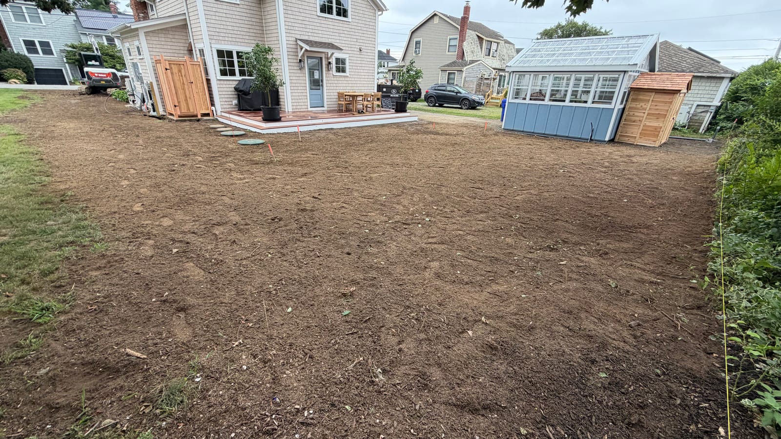 Final grade raked out across a Warren, RI backyard prepped for 2,600 sq ft of sod, with the shingled house, back porch, and greenhouse behind