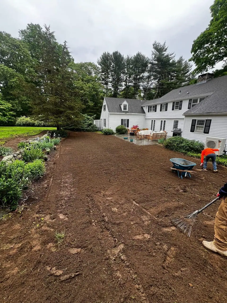 Hand-raking the soil to a finish grade along a stone patio edge in Westbrook, CT before laying sod
