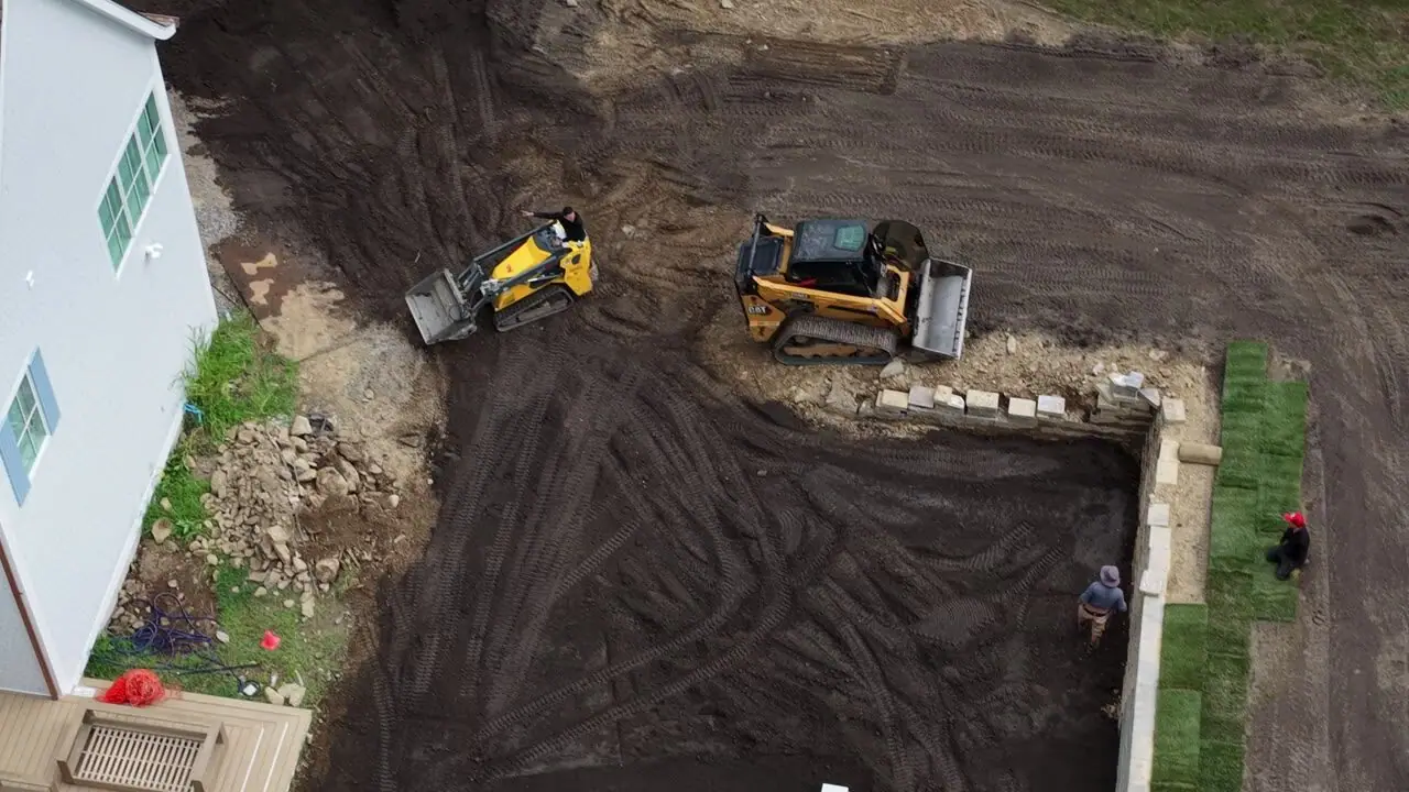 Over the roofline to the back corner — the loader tightens the working edge while the first courses hold the fence line