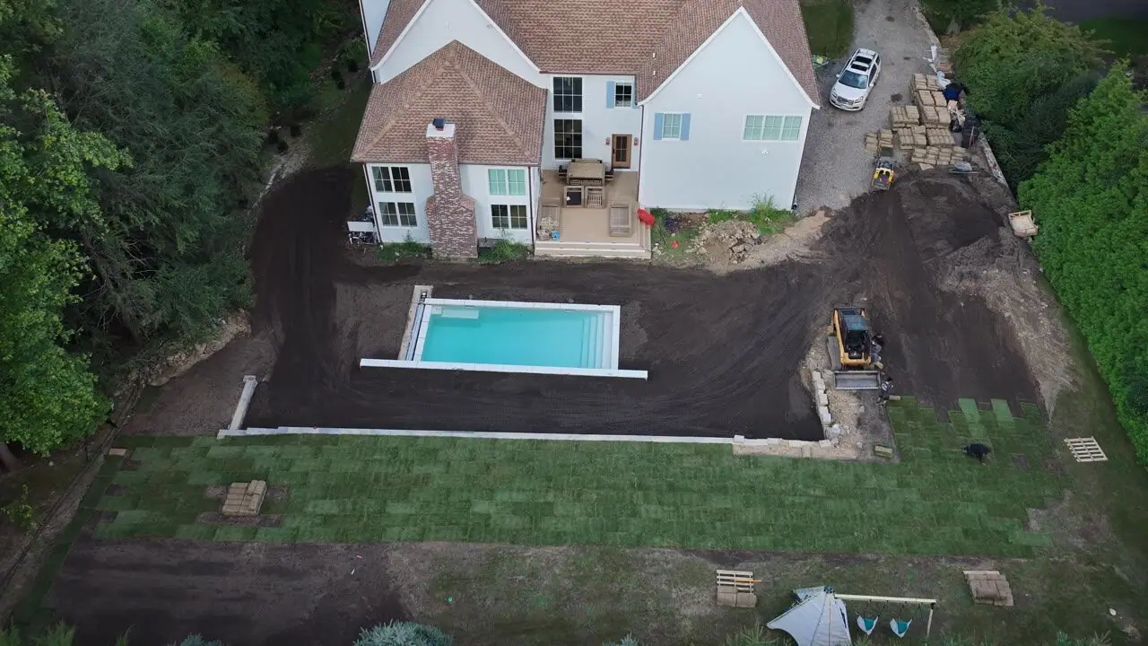 Fresh sod wrapping the pool apron in the evening light, the crew still working the far side