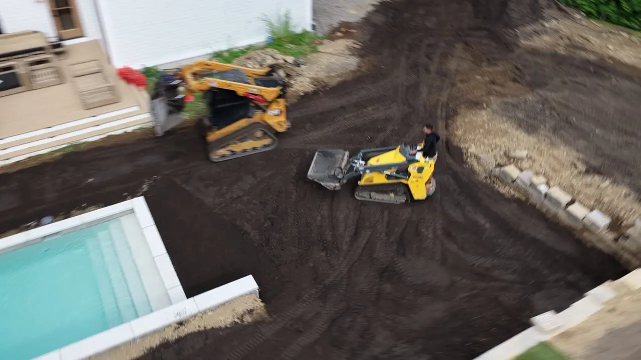 Following the skid steer from the pool corner out to the pallet rows staged by the garage