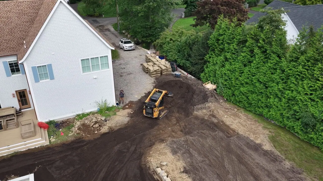A quick hover at the front corner as the loader tightens the last of the grade beside the porch