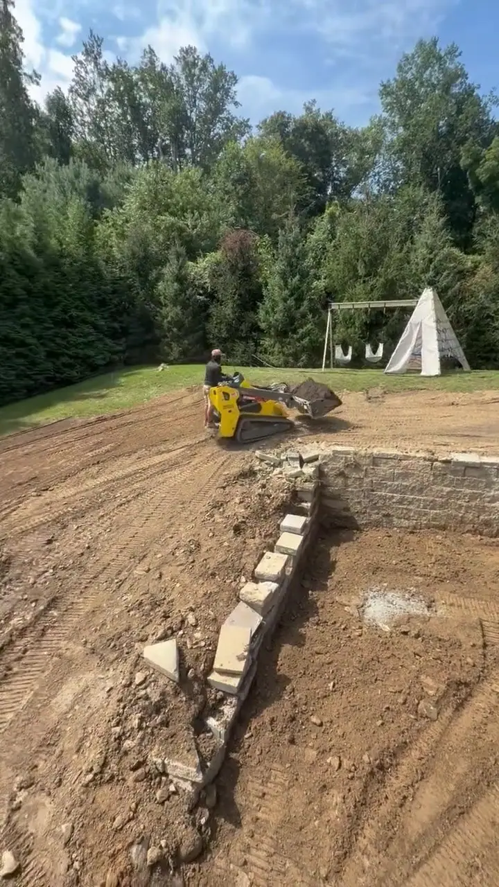 Late Friday morning in Westport — the excavator working the exposed lower-yard grade, with the separate pool construction beside the future lawn area
