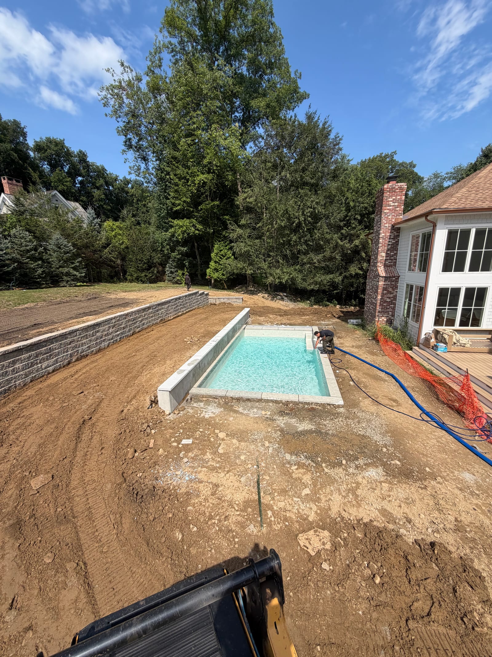 Late-morning view across the Westport backyard with the excavator working beside the separate pool build and rough lower-yard grade exposed