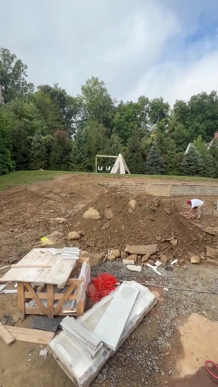 9 a.m. Friday — work underway in the lower yard: rock and construction fill that has to be hauled off before topsoil, with the separate pool build beyond and the established lawn above the retaining wall