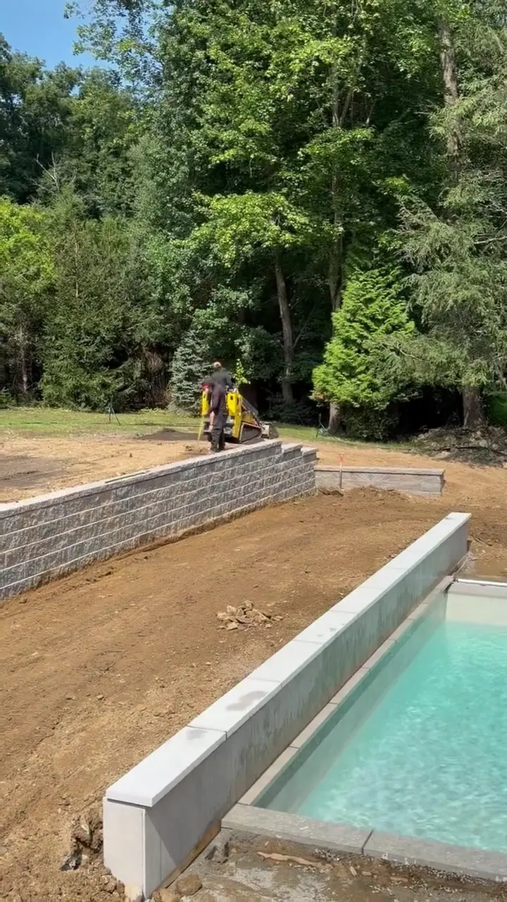 A second late-morning pass around the new wall and pool edge, showing how much machine work sits between the construction subgrade and a lawn-ready finish grade