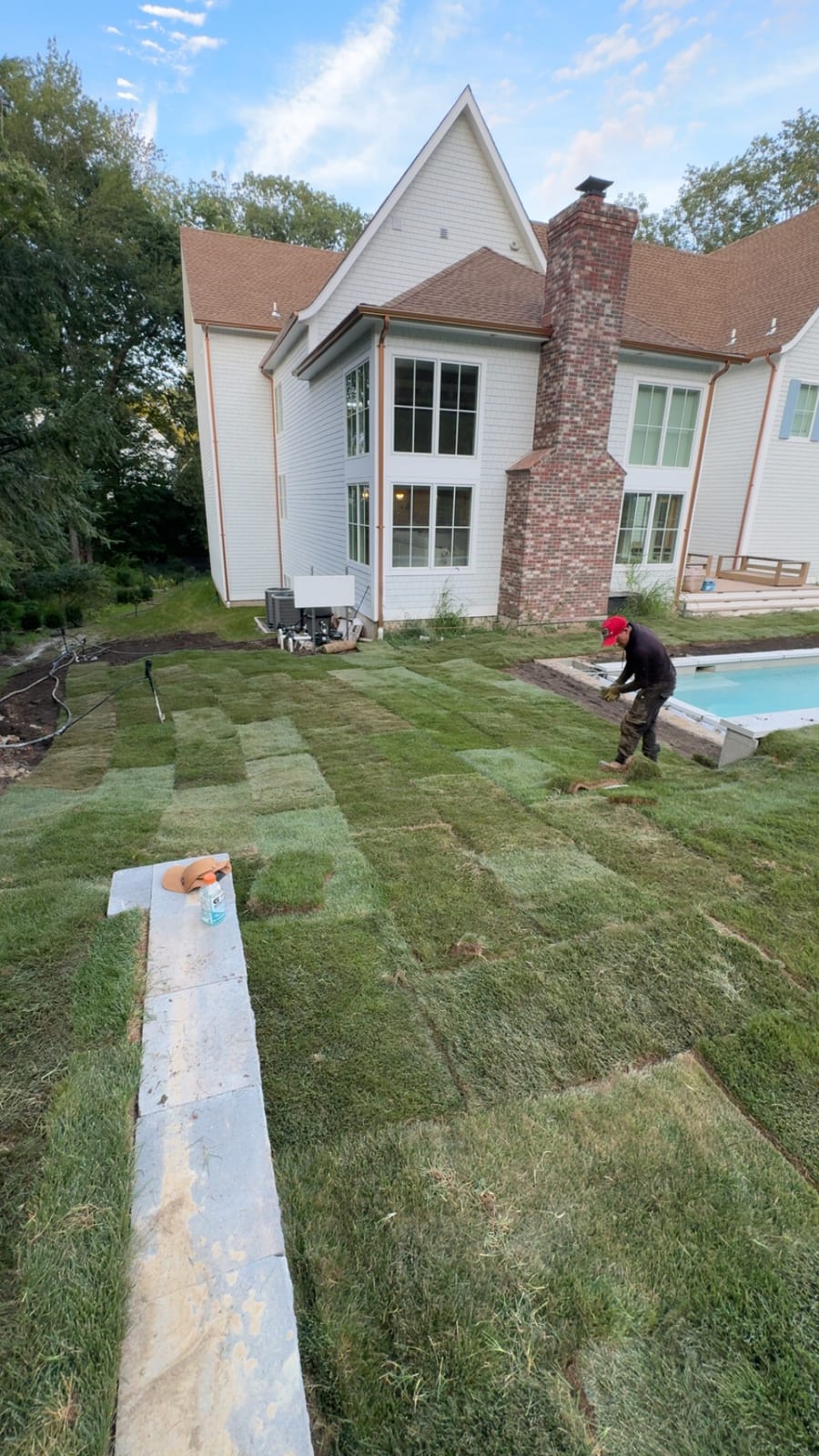 Rows of fresh sod laid behind the Westport house as a crew member places pieces near the pool in fading light
