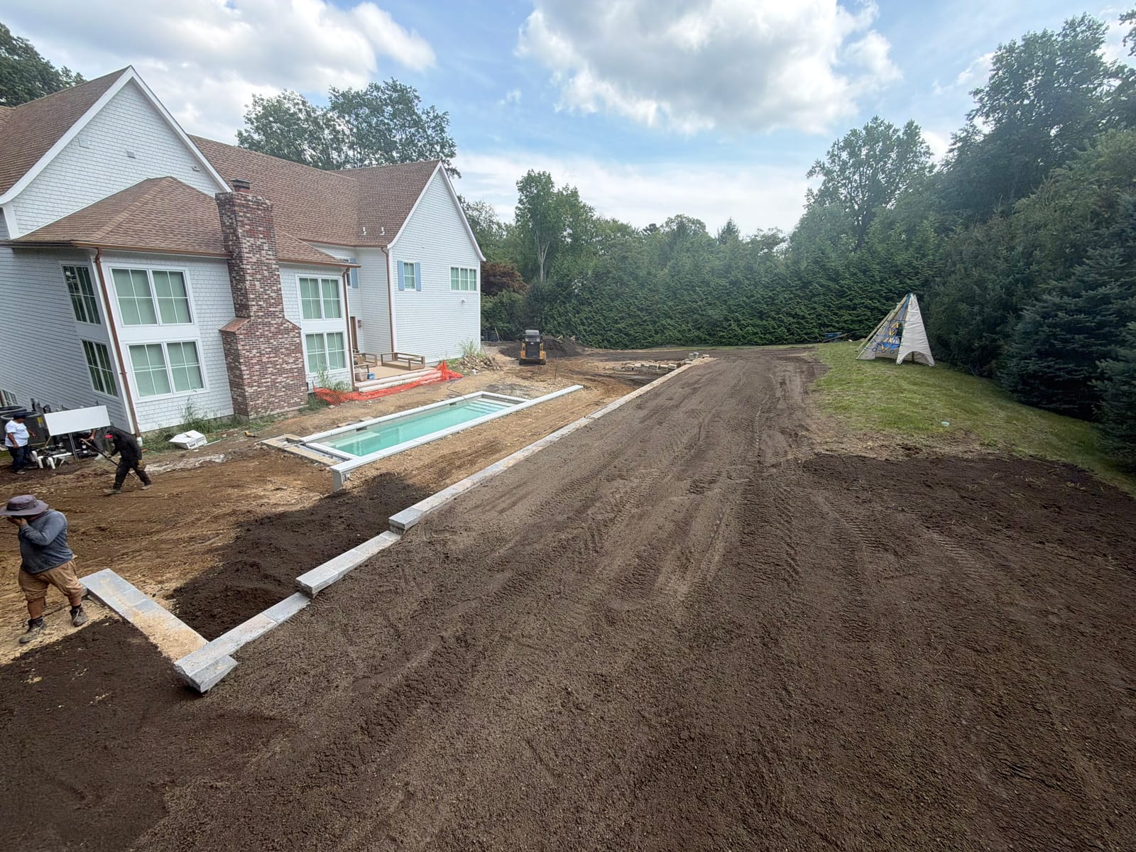 Wide Friday afternoon view of the Westport backyard with screened topsoil spread across the future lawn and the crew refining the grade beside the separate pool build