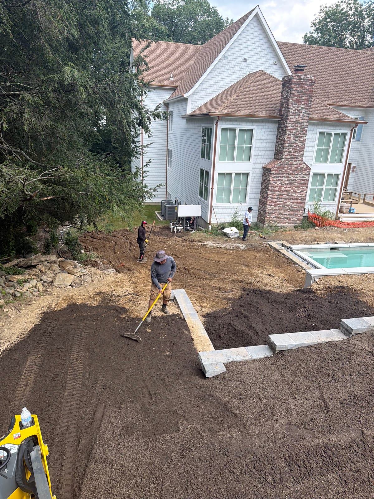 Westport sod crew hand-raking screened topsoil beside the wall and separate pool construction