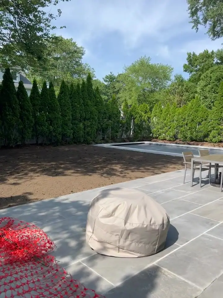 Clean screened topsoil graded around the new pool and stone patio in Fairfield, CT, ready for Kentucky bluegrass sod