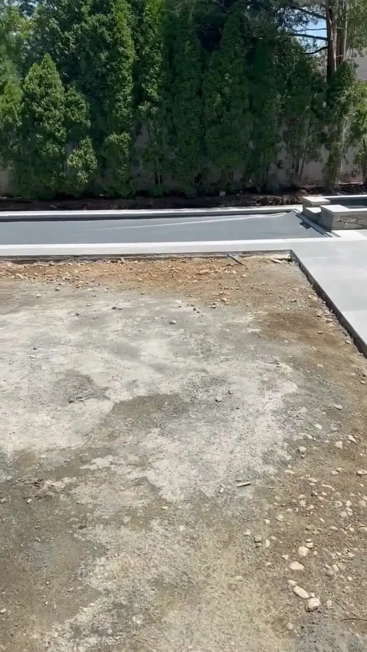 Homeowner walkthrough of a Fairfield, CT backyard as the pool builder left it — thin dusty grade, gravel, and hardened concrete slurry around the new pool and stone patio