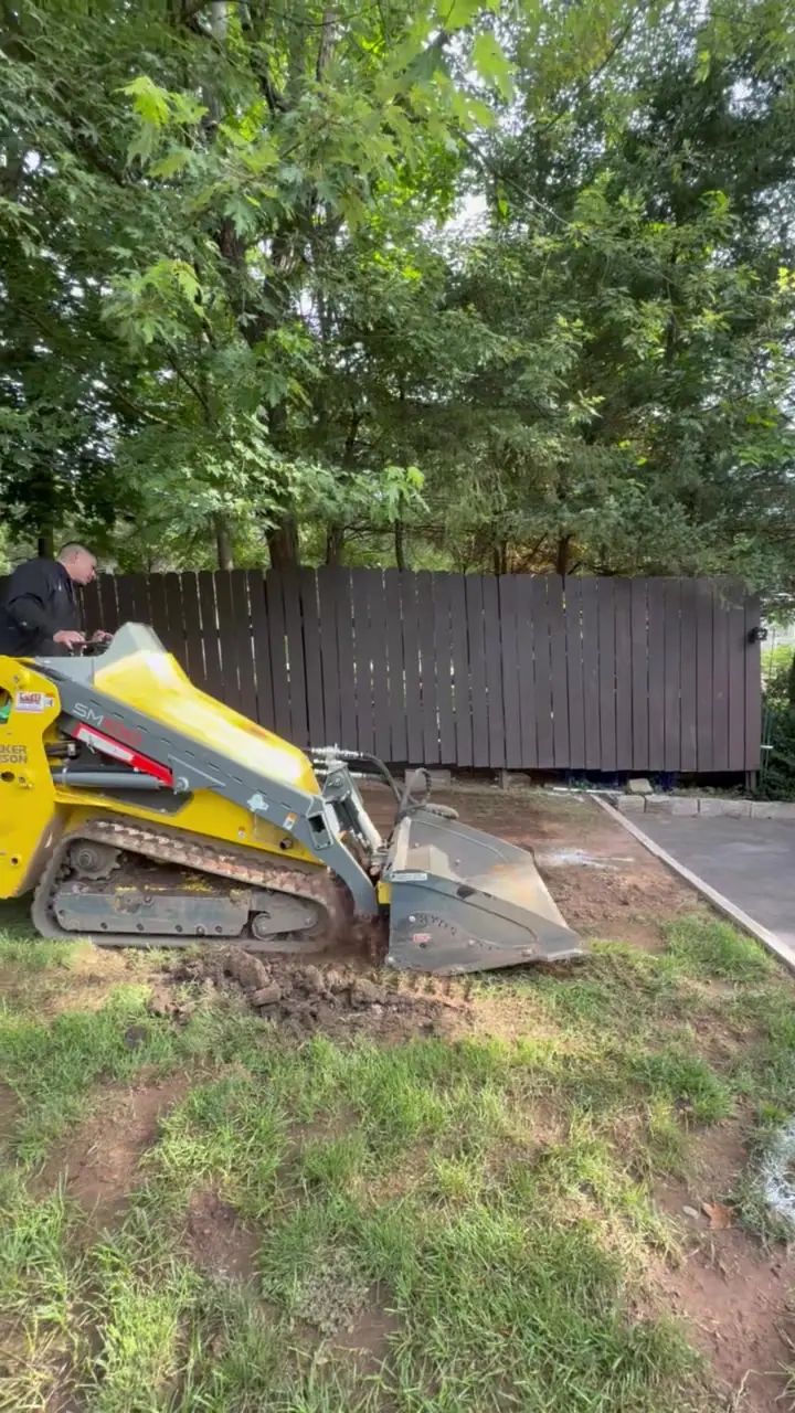 A tracked machine opens and works the damaged lawn during site preparation in Meriden, Connecticut
