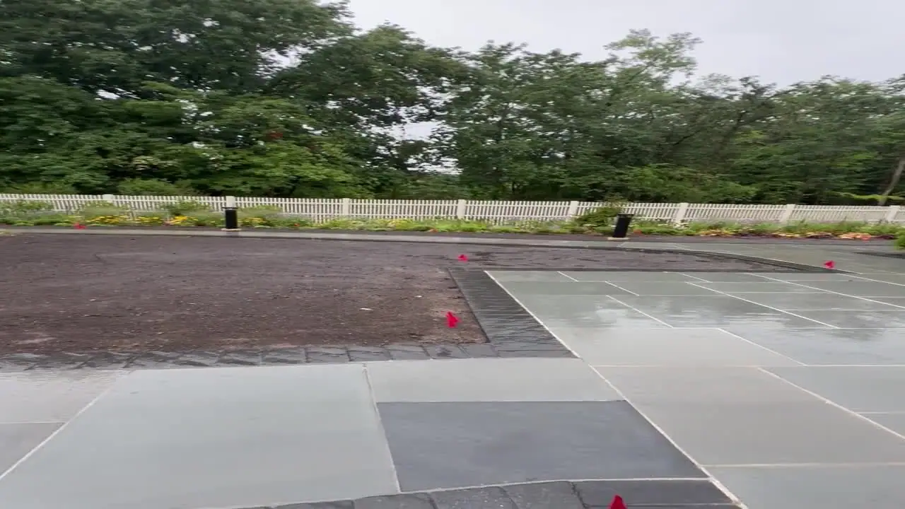 Pan across a rain-soaked commercial property in New Canaan, CT with wet bluestone and bare graded soil hours before a party
