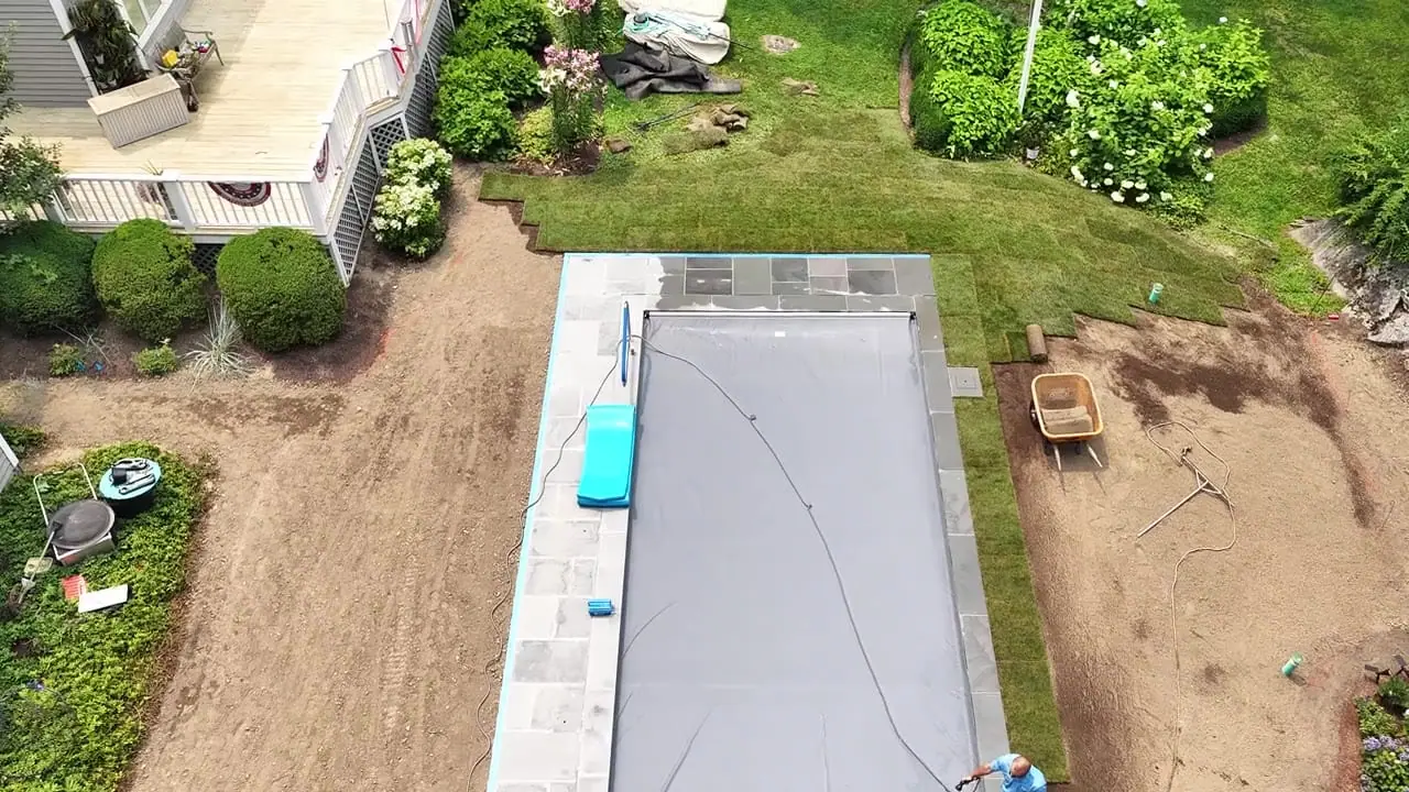 Drone view of the first rolls of fresh sod going down across the graded yard around a new pool in New Canaan, CT
