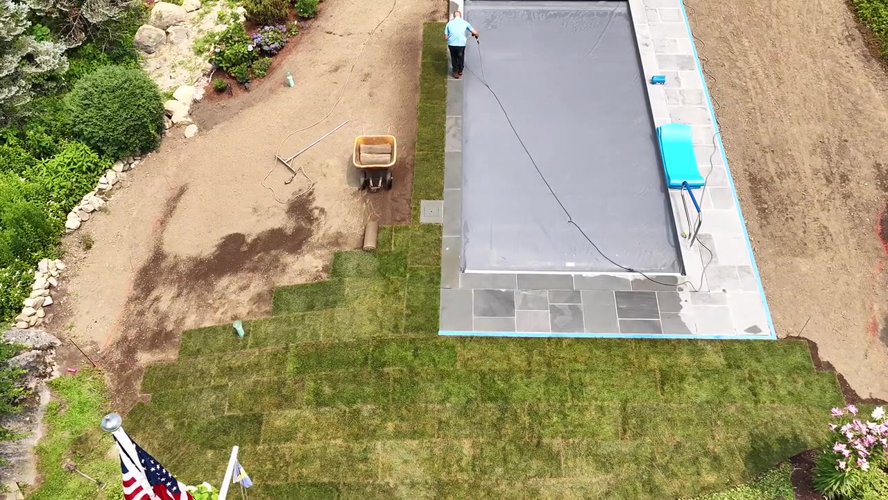 Mid-install flyover — fresh sod already seamed tight to the pool coping at the near end of the yard, with the crew still working the open grade by the planting beds