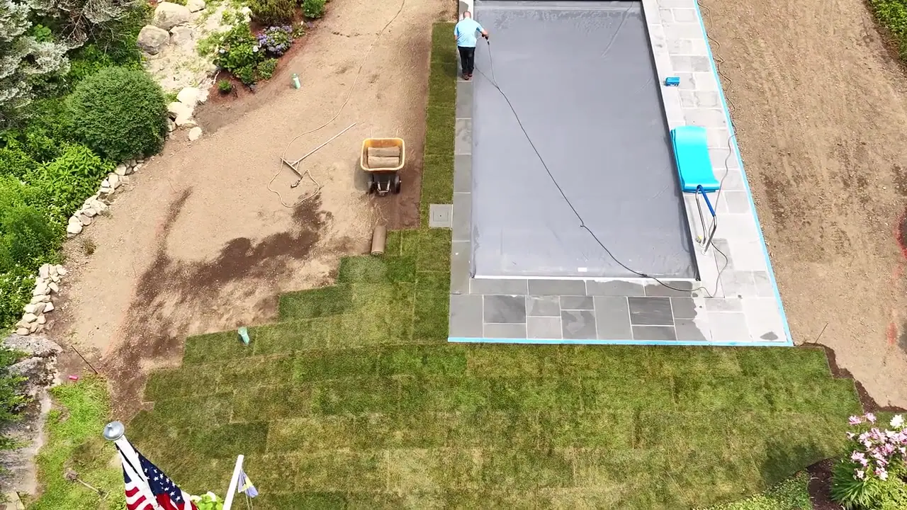Drone flyover mid-install in New Canaan, CT — fresh sod seamed tight to the pool coping while the crew works the open grade by the planting beds