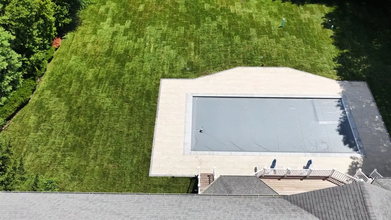 Straight over the pool and patio in Purchase, NY — the new bluegrass runs wall to wall from the coping to the tree line