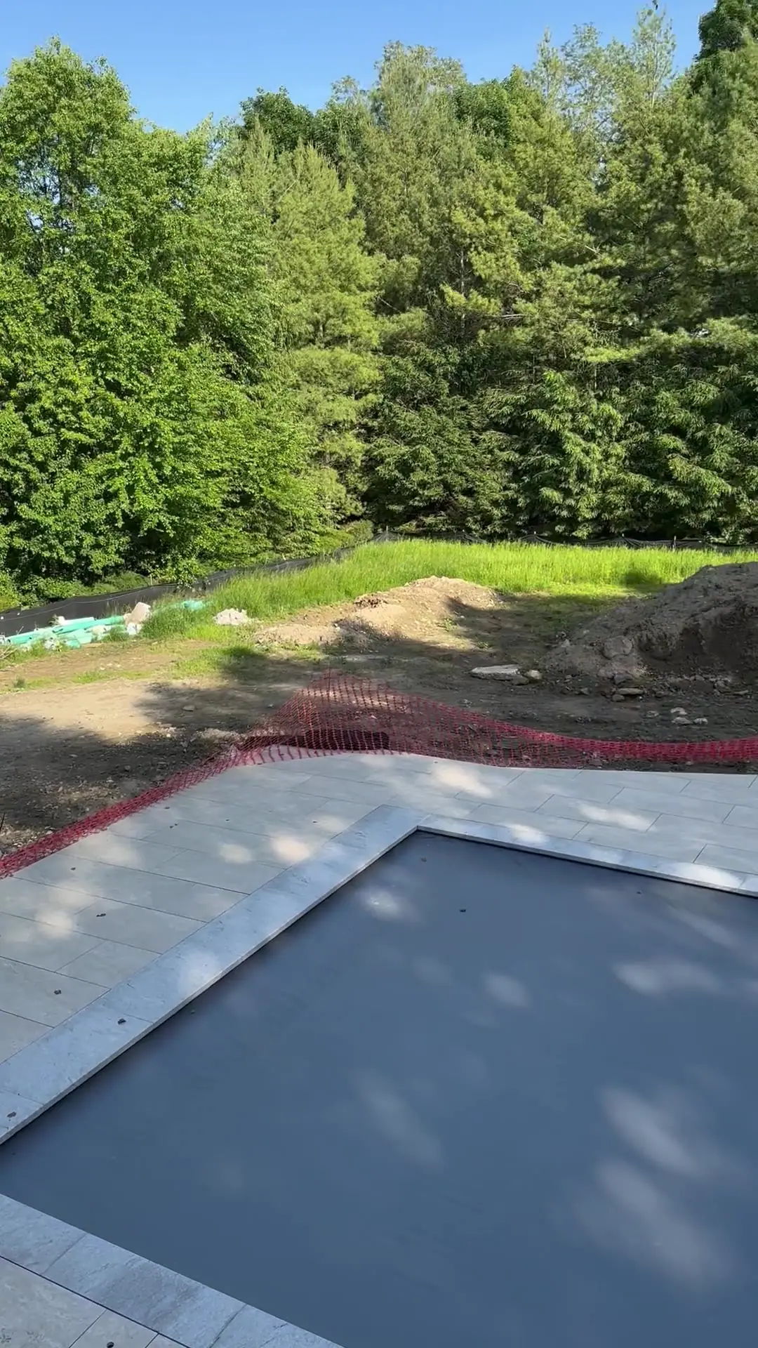The yard mid-project — pool tarped, silt fence up, and the lawn already stripped to dirt by weeks of heavy equipment traffic