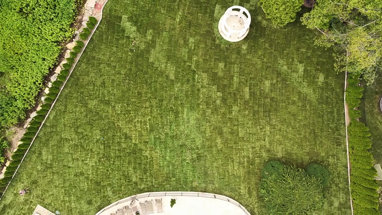 Straight down over the finished lawn — tight checkerboard seams running from the gazebo to the privacy hedges