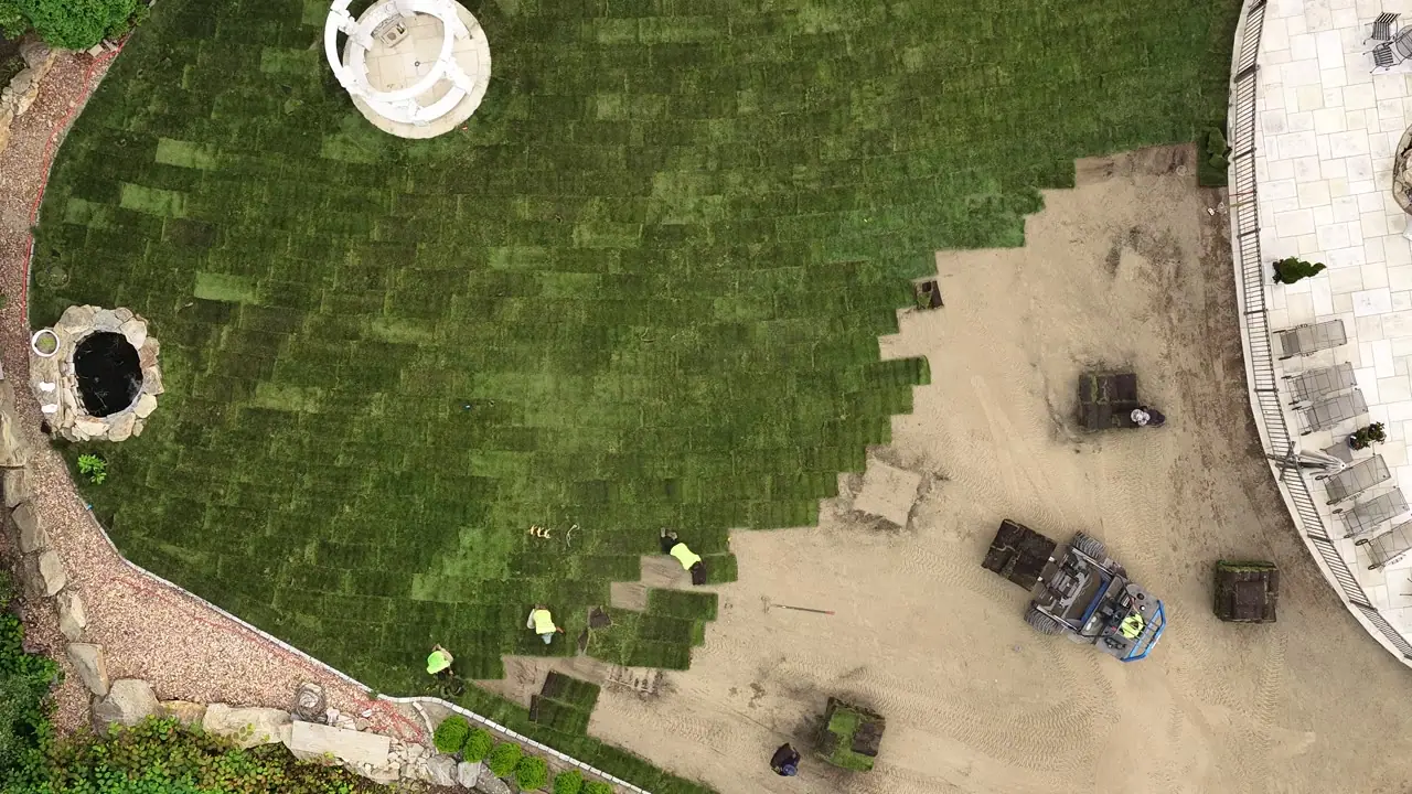 Top-down drone view of staggered sod seams advancing across the graded yard in Shelton, CT, crew and forklift at the working edge