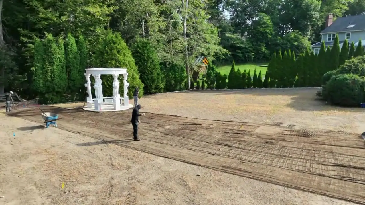 From the pool fence up over the yard — the crew rakes the fresh topsoil smooth around the gazebo while the track loader keeps material coming