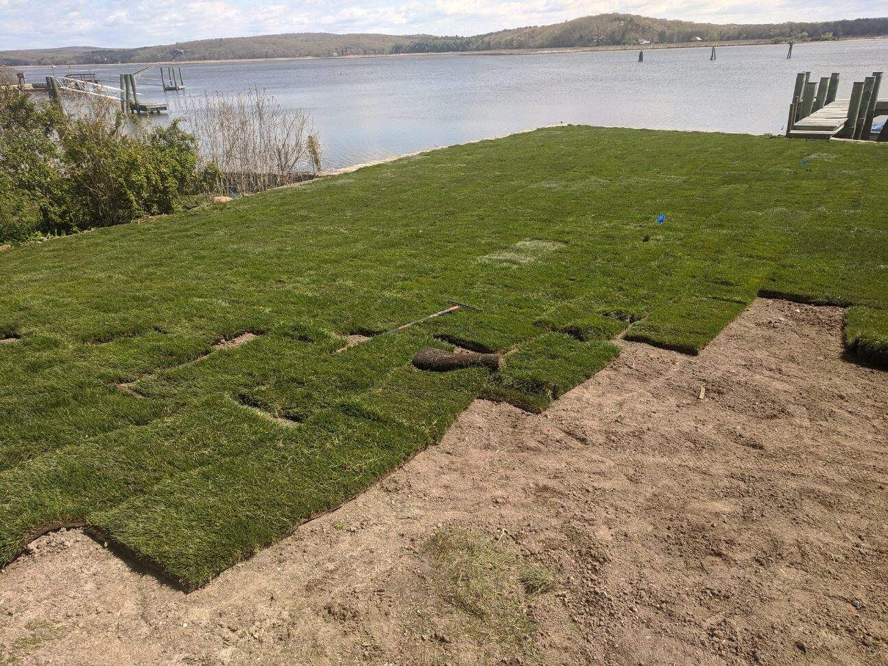 Fresh sod rolls being laid on a waterfront residential property.