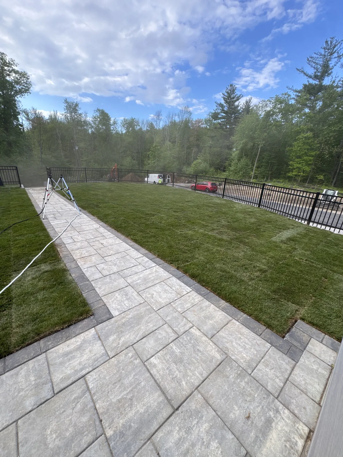Wide view of finished Kentucky Bluegrass sod lawn along paver walkway with black aluminum fence — completed Millbury MA install by CT Sod