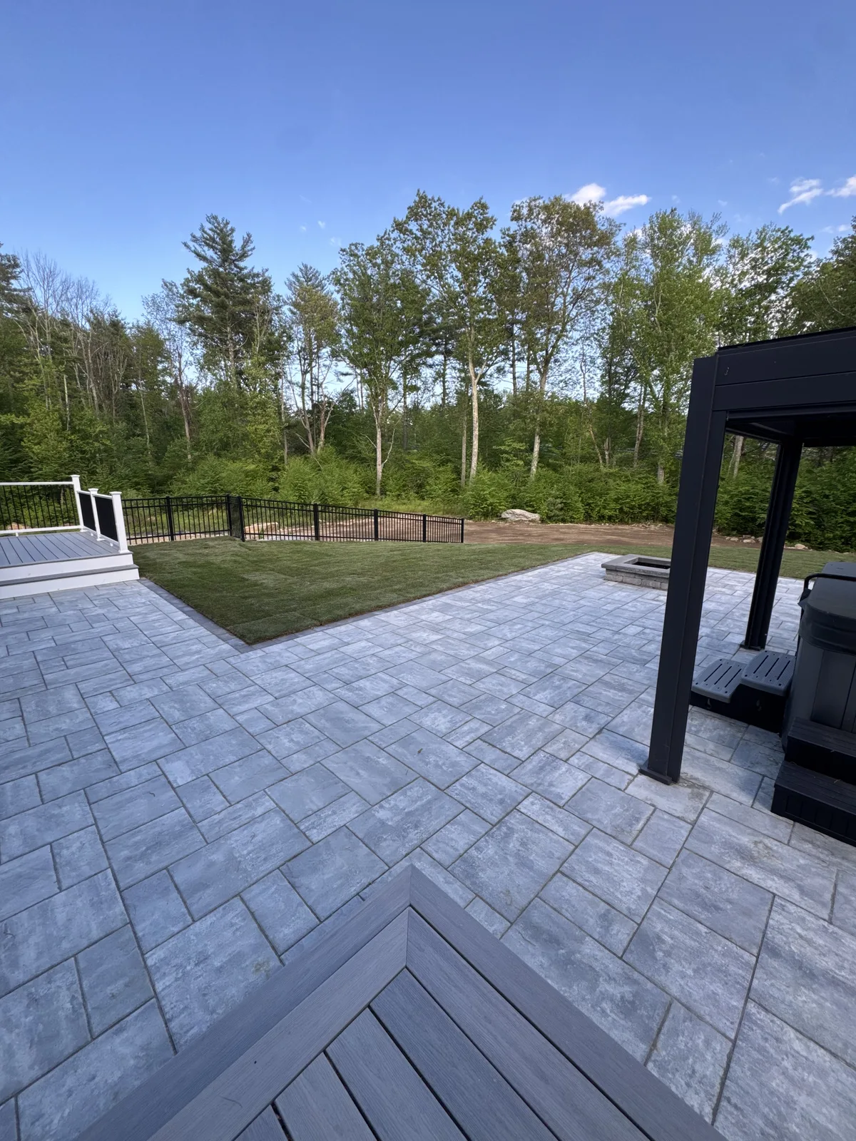 New Kentucky Bluegrass sod installed between composite deck and paver patio with black aluminum fence — Millbury MA backyard sod install