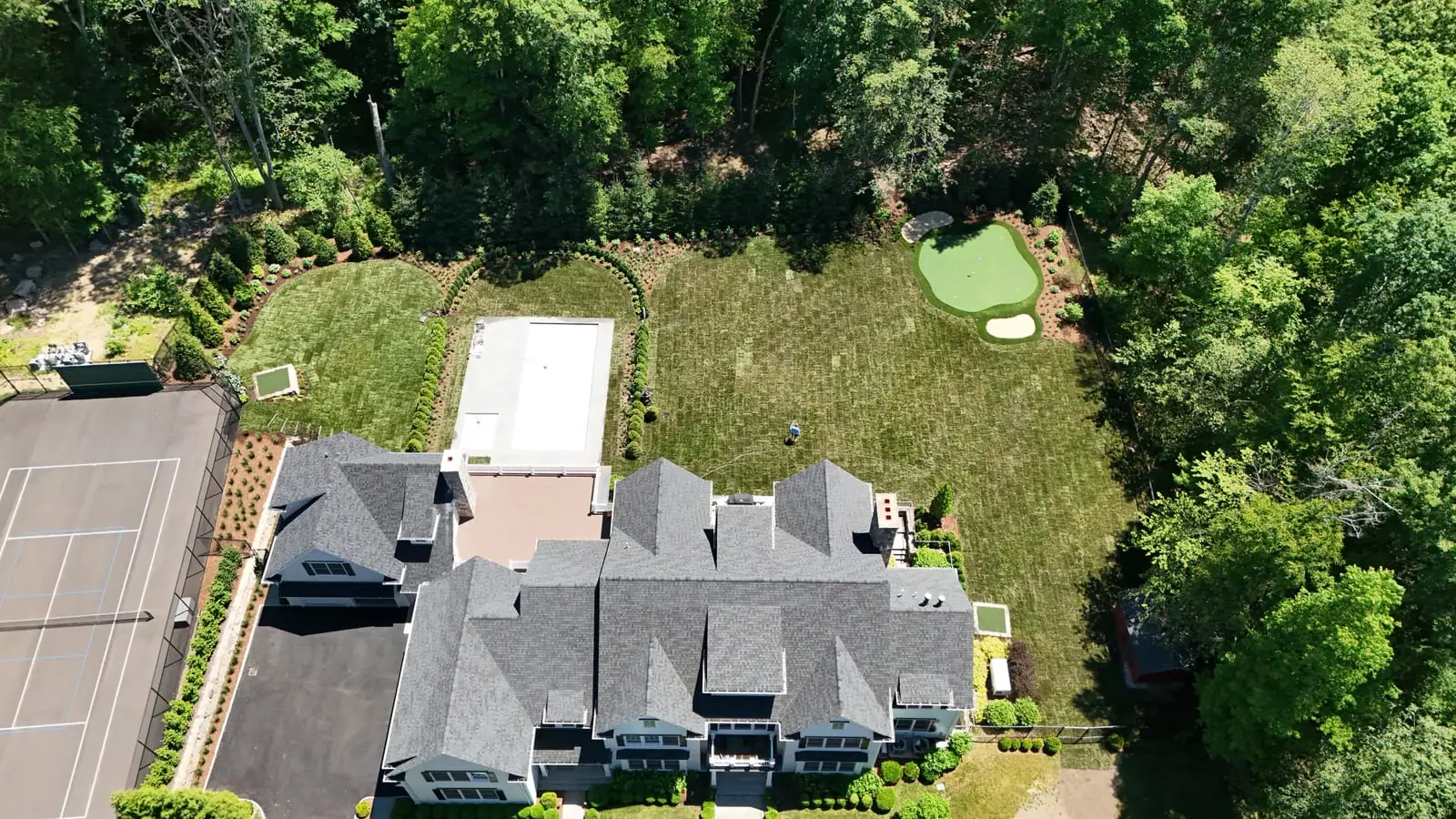 Aerial view of the finished sod lawn across a New Canaan, CT estate backyard, green from the pool out to the putting green and hedge rows