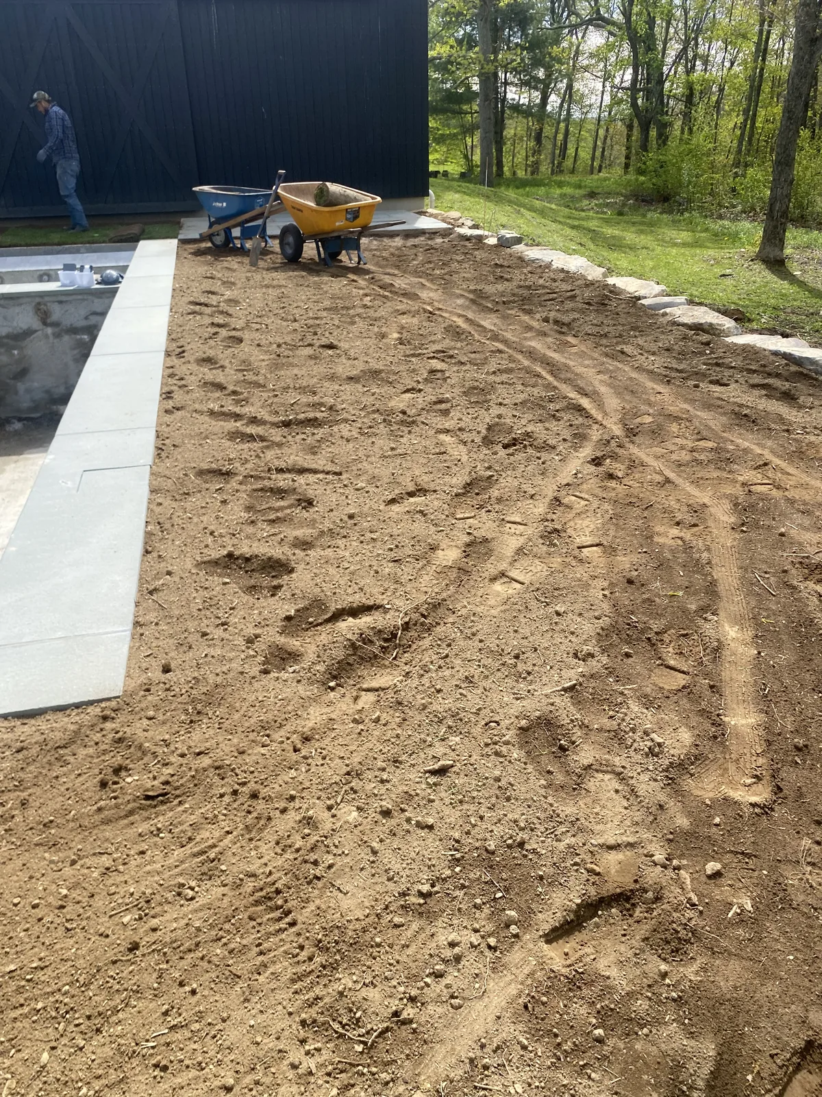Warren CT sod install prep — graded soil around a new pool surround, wheelbarrow staged for the crew