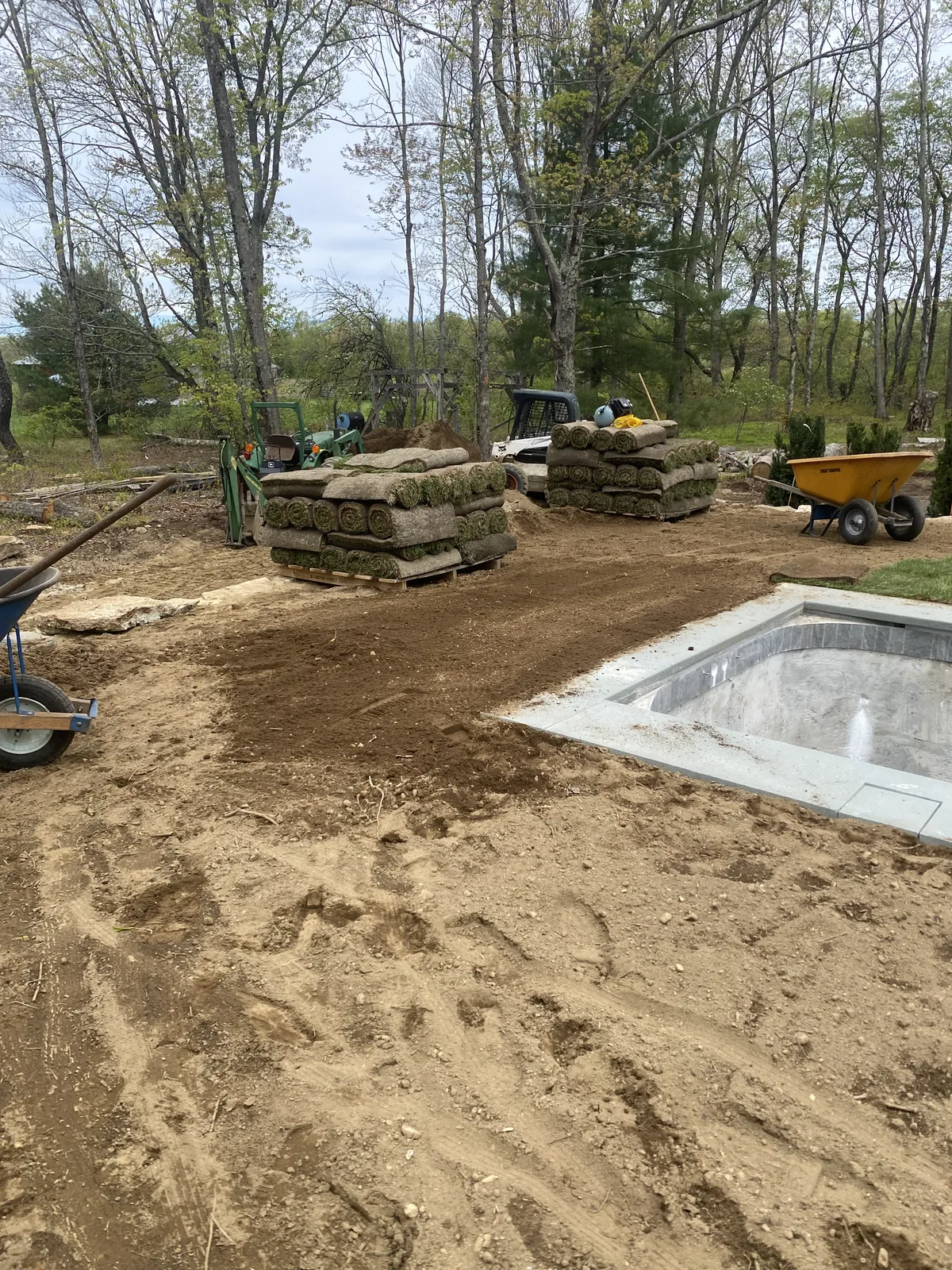 Warren CT sod install — fresh-cut sod pallets staged beside a pool surround with skid steer and all-terrain forklift on a Litchfield County estate