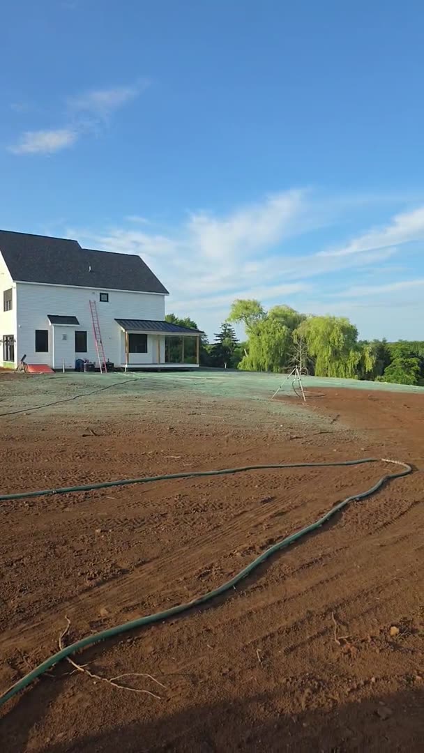 A freshly graded and raked lawn bed prepped for hydroseeding, with irrigation hoses and sprinkler tripods staged across the site