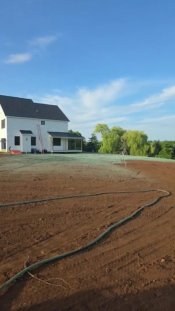 A freshly graded and raked lawn bed prepped for hydroseeding, with irrigation hoses and sprinkler tripods staged across the site