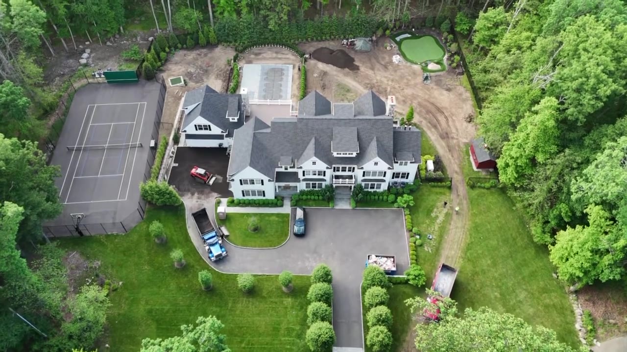 Drone fly-over of a New Canaan, CT estate during sod prep — regraded lawn areas, putting green, tennis court, and dump trucks staged for fresh-cut sod delivery