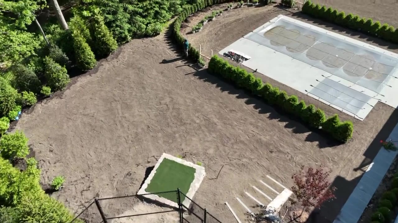 Drone fly-over of the rear yard of a New Canaan, CT estate finishing sod prep — graded soil around the pool, putting green, and hedge rows after spreading fresh topsoil