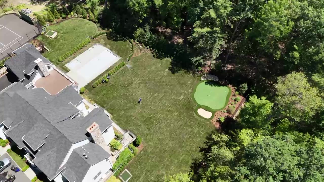 Drone flyover of a New Canaan, CT estate backyard after sod installation — freshly laid sod across the full lawn around the pool and putting green