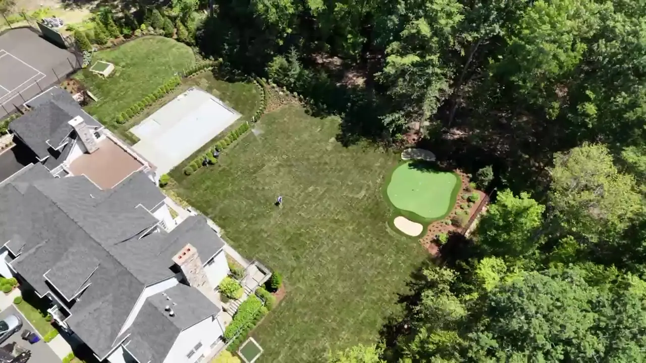 Drone flyover of a New Canaan, CT estate backyard after sod installation — freshly laid sod across the full lawn around the pool and putting green